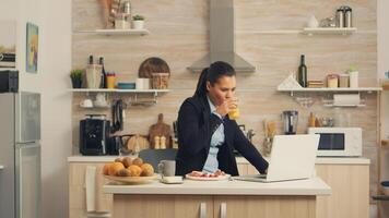 Business woman eating breakfast and working on laptop. Concentrated business woman in the morning multitasking in the kitchen before going to the office, stressful way of life, career and goals to meet photo