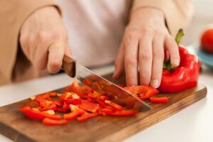 Woman cutting bell pepper on cutting board for salad in kitchen. photo