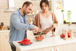 hombre torrencial aceituna petróleo en ensalada en cocina. sano ensalada con Fresco vegetales. contento en amor alegre y despreocupado Pareja Ayudar cada otro a preparar comida foto