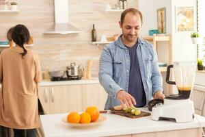 Guy preparing tasty smoothie in kitchen using blender. Healthy carefree and cheerful lifestyle, eating diet and preparing breakfast in cozy sunny morning photo