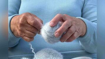 A woman with knitting in her hands. The hands of an old woman at needlework. A woman in blue dissolves a woolen scarf. Knitting concept, retired tranquil carefree life . video