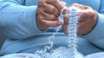 une femme avec tricot dans sa mains. le mains de un vieux femme à travaux d'aiguille. une femme dans bleu dissout une de laine foulard. tricot concept, retraité tranquille insouciant la vie . video