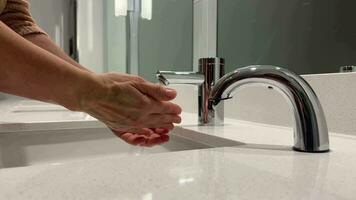 Hand washing. White washbasin and faucet on granite counter with hand washing. A woman washes her hands with soap foam. Touch dispenser with soap foam for hands. video