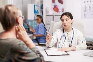 Senior woman having problem with sore neck. Young doctor wearing white coat and stethoscope during examination of old patient. photo