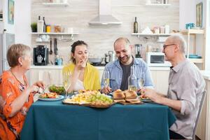 Multi generation family smiling during lunch enjoying tasty potatoes and telling jokes. Tasty roasted potatoes on dining table. photo