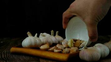 A man's hand pours garlic cloves onto a wooden plate. video