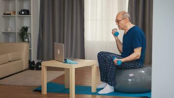 Senior man training in living room with dumbbells during online fitness program. Old person pensioner healthy training healthcare sport at home, exercising fitness activity at elderly age photo