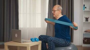 Senior man with vitality doing fitness exercise with resistance band watching online program. Old person pensioner healthy training healthcare sport at home, exercising fitness activity at elderly age photo