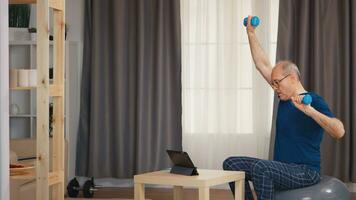 Grandfather training in living room with dumbbells watching online fitness program. Old person pensioner healthy training healthcare sport at home, exercising fitness activity at elderly age photo