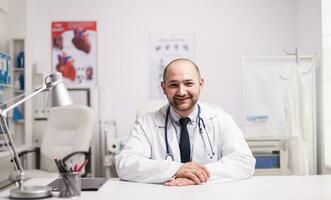 Portrait of successful young doctor in hospital office wearing white coat smiling at camera. photo