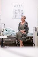 Senior woman with glasses in hospital office waiting for doctor. photo