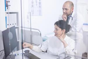Young couple of doctors analysing medical scan on computer discovering the right treatment. Cardiologist showing and explaining results to his colleague using personal computer photo