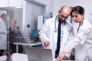 Worried team of young doctors pointing on laptop anlysing result of patient discussing healh problems. Doctor showing and explaining treatment to his colleague using personal computer photo