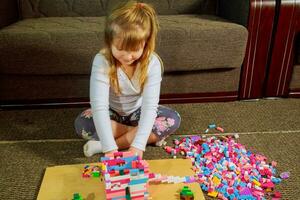 Child girl having fun and build of bright plastic construction blocks. photo