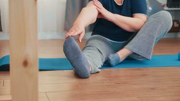 Old woman stretching sitting on yoga mat in living room. Old person pensioner exercise training at home sport activity at elderly retirement age photo