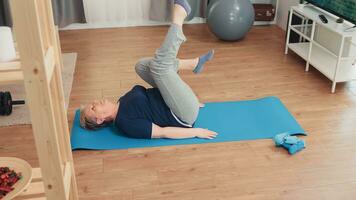 Elderly age woman exercising sitting on yoga mat in living room. Old person pensioner exercise training at home sport activity at elderly retirement age photo