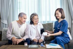 Senior couple get medical service visit from caregiver nurse at home while having blood pressure test using sphygmomanometer on for health care and pension welfare insurance concept photo