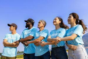 Team of young and diversity volunteer workers group enjoy charitable social work outdoor in the beach cleaning project wearing blue t-shirt while joining hand in assemble unity photo