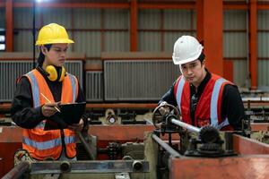 Team of Asian industrial worker is checking the setup value of metal sheet roll forming machine by automated monitor while working inside roof factory for safety industry photo