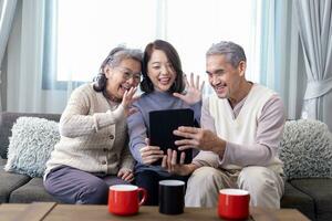 Asian family reunion of senior father mother and daughter sitting on couch with happy smile in retirement home while having video call to others relation and cousin member photo