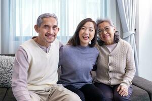 Asian family portrait consist of senior father mother and daughter sitting together with happy smile on the cozy couch in retirement home during winter for elder care to spending valuable time photo