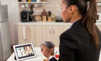 mujer de negocios en el Mañana teniendo un en línea conferencia llamada mientras comiendo desayuno en el cocina. foto