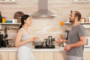 Husband playing with an orange and talking with his wife in the kitchen. Husband having a conversation with wife while she is preparing eggs for breakfast. photo