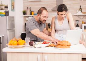 Husband and wife reading a mail on laptop in the morning during breakfast. Married husband and wife in pajamas using internet web online modern technology, smiling and happy in the morning. Reading news browsing internet photo