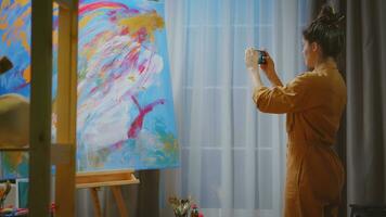 Innovative woman painter taking photo of her masterpiece in art studio.