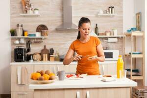 Cheerful woman in the morning singing and spreading butter on roasted bread. Knife smearing soft butter on slice of bread. Healthy lifestyle, making morning delicious meal in cozy kitchen. Traditional tasty lunch photo