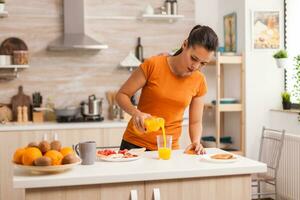 esposa torrencial Fresco jugo en vaso para desayuno en cocina. mujer Bebiendo sano y natural naranja jugo. ama de casa Bebiendo saludable, natural, hecho en casa naranja jugo. refrescante domingo Mañana foto