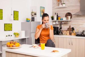 Taking a sip of coffee in the morning while enjoying delicious breakfast. Lady ejoying a cup of coffee in the morning. Happy housewife relaxing and spoiling herself with a healthy meal alone photo