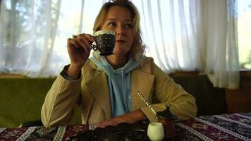 mujer torrencial turco café desde cezve dentro taza. de cerca lento movimiento Disparo de hembra mano con taza en cuadrado lámina, en mesa en café exterior. tradicional caliente sin filtrar café servido en restaurante video