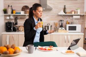 Businesswoman having an online meeting in the morning. Freelancer reading the last news online before going to work, using modern technology in the kitchen while eating a healthy meal. photo