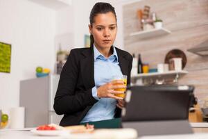 Business woman satisfied to the online project. Business woman reading the project online before going to work, using modern technology in the kitchen while eating a healthy meal photo