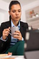 portret de negocio mujer acecho en tableta y Bebiendo un taza de café. persona de libre dedicación leyendo el último Noticias en línea antes de yendo a trabajar, utilizando moderno tecnología en el cocina mientras comiendo un sano comida foto