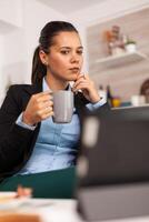 Freelancer drinking coffee in the morning on table top during breakfast using tablet computer. Business woman reading the last news online before going to work, using modern technology in the kitchen while eating a healthy meal photo
