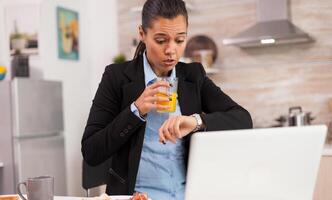 Freelancer late at work while eating breakfast in a hurry. Concentrated business woman in the morning multitasking in the kitchen before going to the office, stressful way of life, career and goals to meet photo