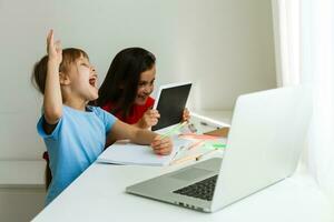 Cool online school. Kids studying online at home using a laptop. Cheerful young little girls using laptop computer studying through online e-learning system. Distance or remote learning photo