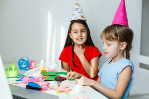 A little girl, curves and laughs in front of a laptop in a cap. Celebrates birthday via internet in quarantine time, self-isolation and family values, online birthday. Congratulations to the animator photo