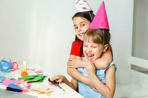 un pequeño chica, curvas y se ríe en frente de un ordenador portátil en un gorra. celebra cumpleaños vía Internet en cuarentena tiempo, autoaislamiento y familia valores, en línea cumpleaños. Felicidades a el animador foto