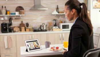 Business woman during a video call with friends while eating breakfast before leaving to the office. Using modern online internet web technology to chat via webcam videoconference app with relatives, family, friends and coworkers photo