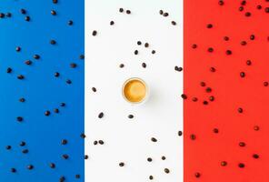 Creative layout made of cup of coffee and coffee beans on flag of France as a background. Minimal coffee concept. Trendy espresso idea. Unique flat lay composition. Coffee aesthetic. photo