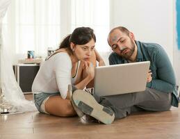 Tired couple using laptop during apartment renovation sitting on the floor. Apartment redecoration and home construction while renovating and improving. Repair and decorating. photo