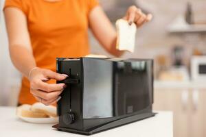 Woman waiting for roasted bread to pop from electric toaster. Housewife using bread toaster for delicious breakfast. Healthy morning in cozy interior, delicious home meal preparation photo