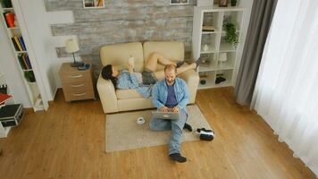 Husband and wife enjoying some free time on a sunday afternoon, he is browsing on the laptop while she reads photo