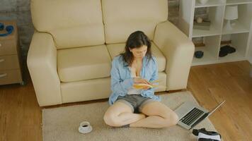 Top view of woman in short jeans reading a book with a cup of coffee and a laptop next to her photo