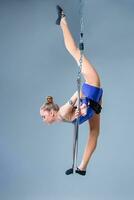 Young woman hanging in aerial ring on a blue background photo