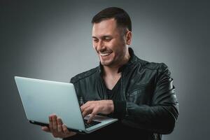 Man in black jacket looking at laptop, half turn. Holding opened laptop and working. Emotion. photo