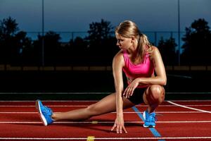 atractivo joven mujer atleta extensión piernas en estadio foto